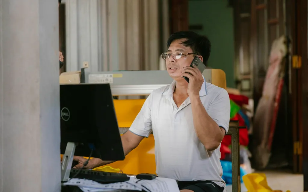 A tradesman in glasses taking a call on a mobile phone at his workbench