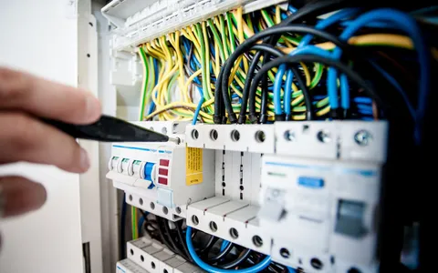 Electrician working on an open consumer unit with coloured wiring and circuit breakers
