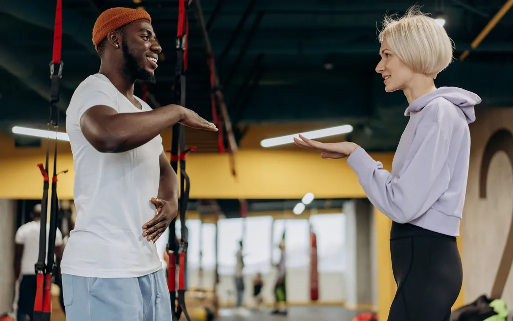 A personal trainer coaching a client on the floor of a bright modern gym