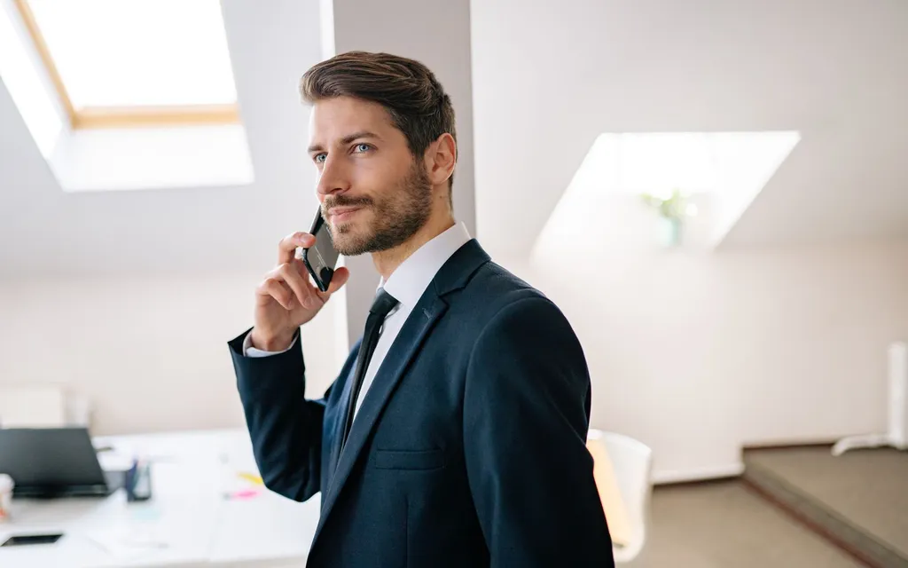 Mortgage broker in a suit talking to a client on the phone in a bright office