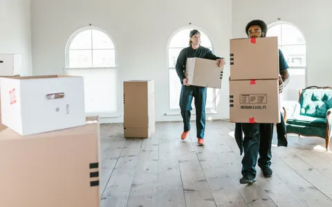 Removals crew carrying cardboard boxes through a bright empty room
