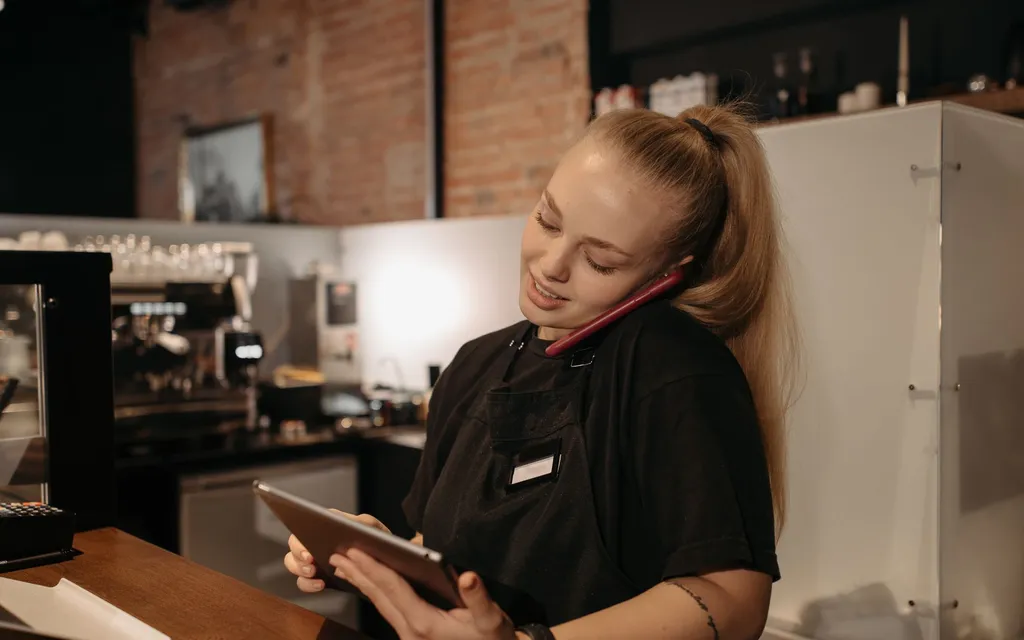 A café team member taking a call at the counter while checking a tablet