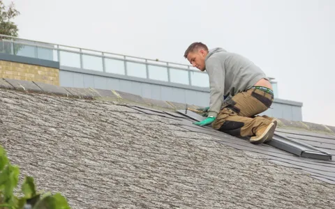 Roofer kneeling on a pitched roof hammering a slate into place
