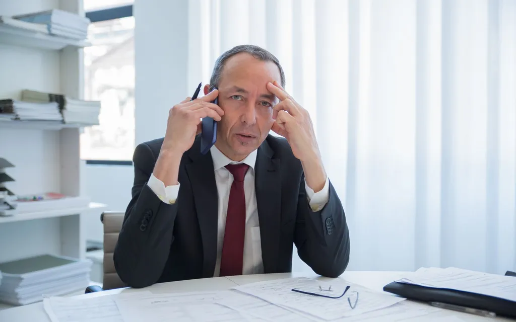 Solicitor in a dark suit taking a call on the phone at a desk of legal documents